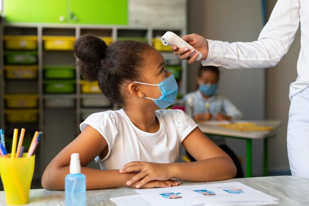 Enseignant sur le côté prenant la température d'un élève