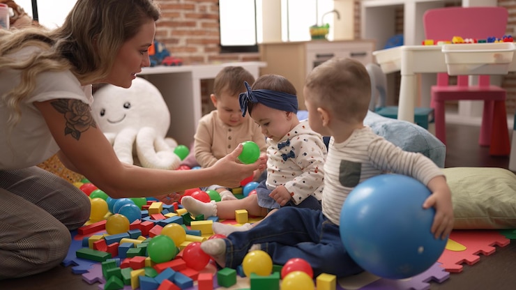Photo gratuit enseignant et élèves d'âge préscolaire jouant avec des balles assis sur le sol à la maternelle