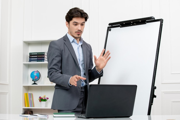 Enseignant instructeur intelligent en costume gris en classe avec ordinateur et tableau blanc expliquant la conférence