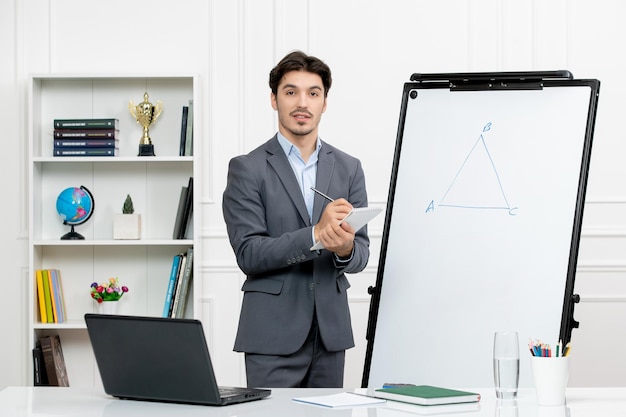 Enseignant jeune instructeur en costume de bureau dans la classe avec des notes d'écriture d'ordinateur et de tableau blanc