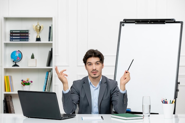 Enseignant jeune instructeur en costume de bureau dans la classe avec ordinateur et tableau blanc tenant un stylo