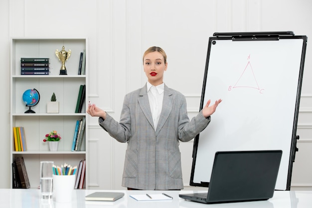 Enseignant jeune instructeur mignon en costume en classe avec ordinateur portable et tableau blanc agitant les mains