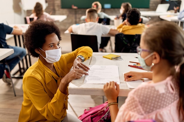 Une enseignante et une écolière afro-américaine portant des masques protecteurs tout en discutant des résultats des tests dans une classe de l'école.