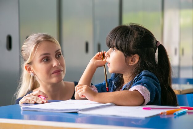 Enseignante sérieuse discutant de la tâche avec petit élève