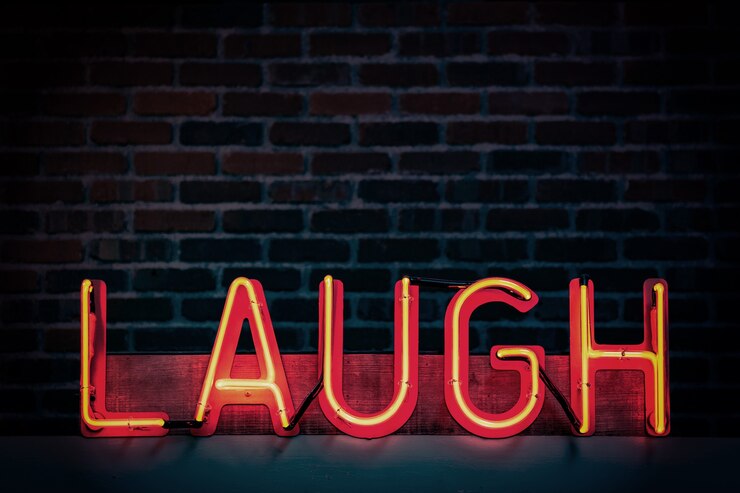 Photo gratuit enseigne au néon rouge qui dit "rire" sur un fond de mur de briques sombres