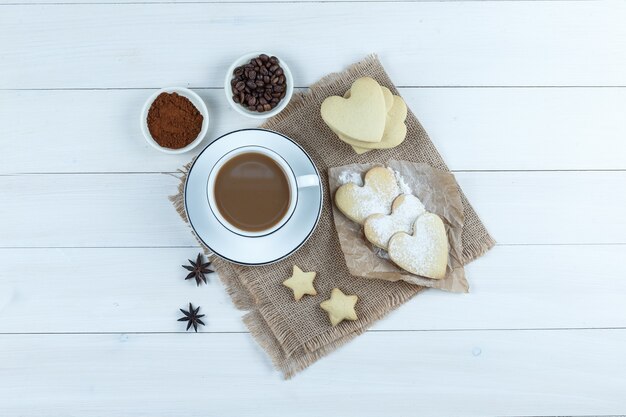 Ensemble de biscuits, épices, grains de café, café moulu et café dans une tasse sur bois et morceau de fond de sac. vue de dessus.