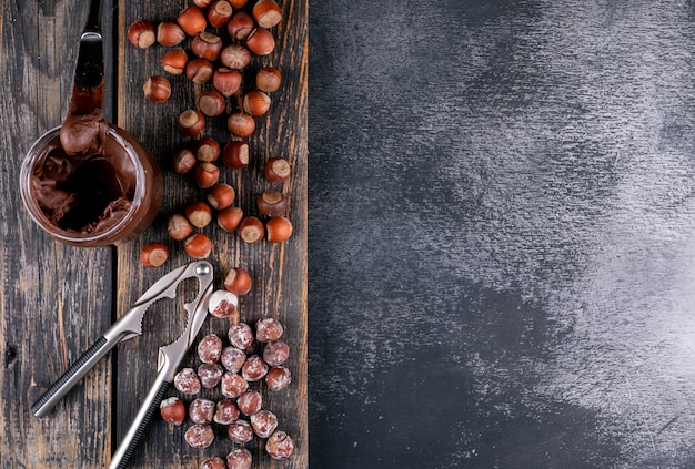 Ensemble de cacao à tartiner et de casse-noisette et de noisettes décortiquées sur une table en bois sombre et pierre noire. vue de dessus.