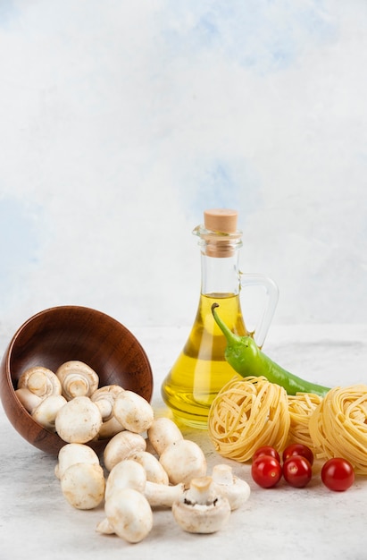 Ensemble de champignons, huile d'olive extra vierge, pâtes, tomates cerises et piments sur un morceau de marbre.