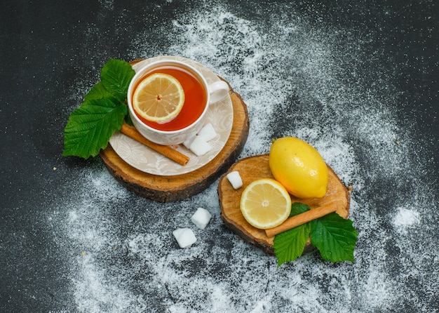 Ensemble de citron, cannelle sèche, morceaux de sucre et une tasse de thé sur des tranches de bois et noir. vue grand angle.