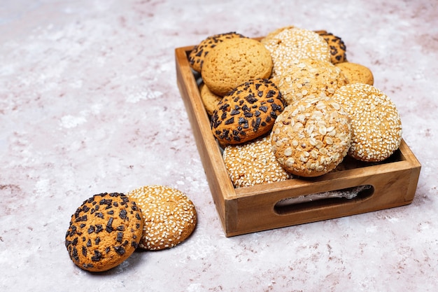 Ensemble de divers biscuits de style américain dans un plateau en bois sur fond de béton clair. Sablés aux graines de sésame, beurre d'arachide, flocons d'avoine et biscuits aux pépites de chocolat.