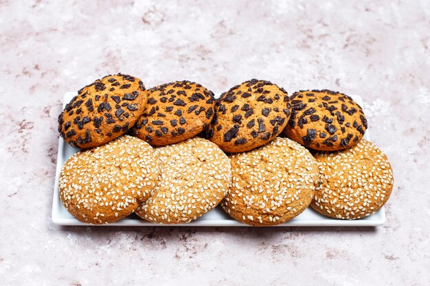 Ensemble de divers cookies de style américain sur un fond de béton clair. Sablés aux confettis, graines de sésame, beurre d'arachide, biscuits à l'avoine et aux pépites de chocolat.