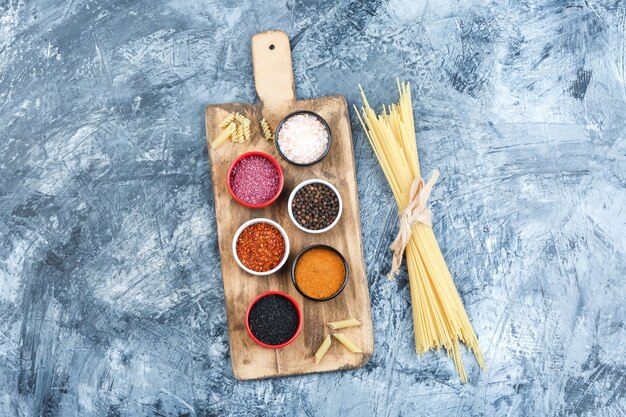 Ensemble d'épices et de spaghettis sur fond de plâtre et planche à découper gris. vue de dessus.