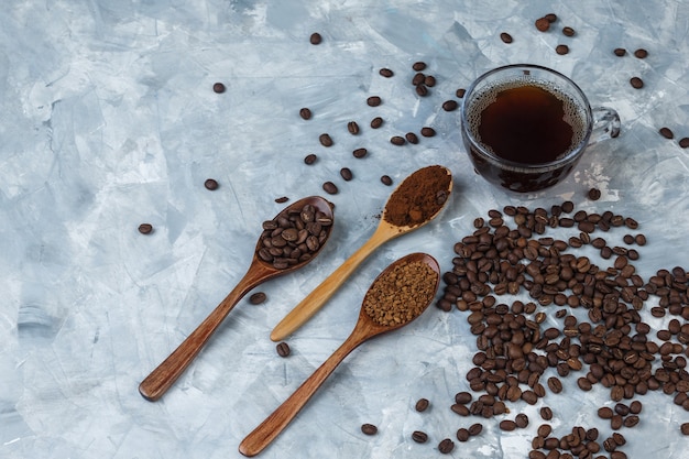 Ensemble de farine de café, café instantané et grains de café dans des cuillères en bois et grains de café, tasse de café sur un fond de marbre bleu clair. fermer.