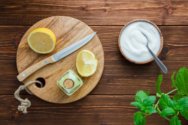 Ensemble de feuilles, couteau en bois, planche à découper, bol de sel et moitié de citron sur une surface en bois. vue de dessus.