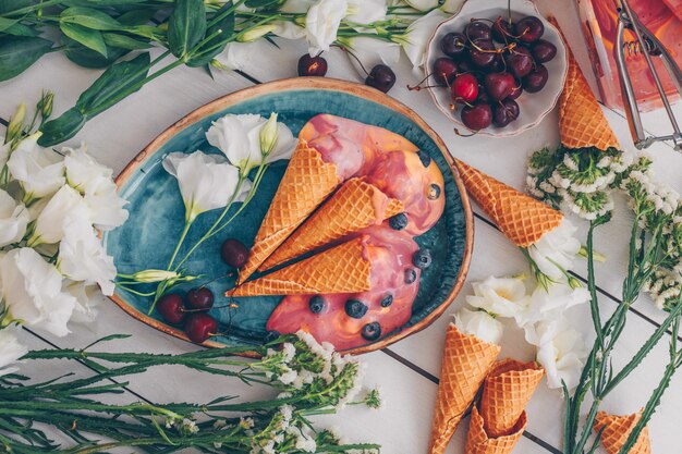 Ensemble de fleurs, fruits et crème glacée en plaque bleue sur bois blanc. vue de dessus.