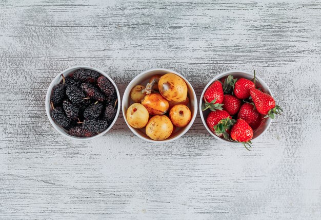 Ensemble de fraises, mûres et nèfles dans des bols sur un fond en bois clair. vue de dessus. espace pour le texte