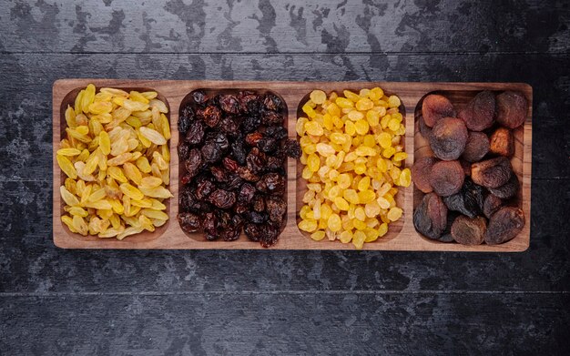 Ensemble de fruits secs raisins cerises et abricots sur un plateau en bois sur fond en bois noir vue de dessus