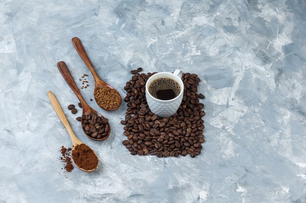 Ensemble de grains de café, café instantané, farine de café dans des cuillères en bois et tasse de café sur un fond de marbre bleu clair. fermer.