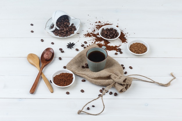 Photo gratuite ensemble de grains de café, café moulu, cuillères en bois et café dans une tasse sur fond en bois et sac. vue grand angle.
