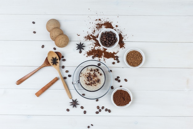 Ensemble de grains de café, café moulu, épices, biscuits, cuillères en bois et café dans une tasse sur un fond en bois. vue de dessus.