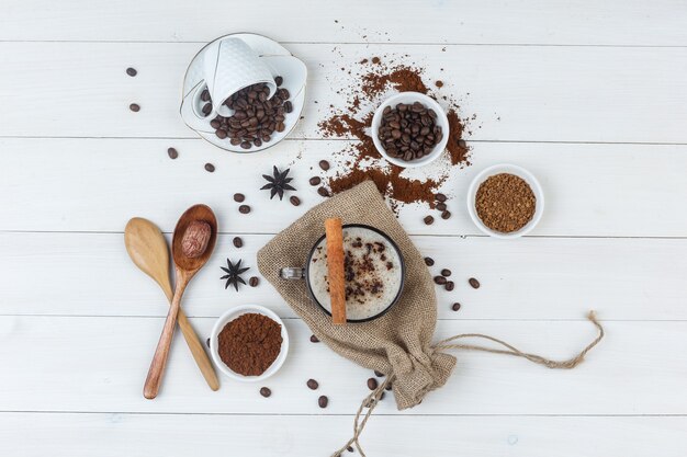 Ensemble de grains de café, café moulu, épices, cuillères en bois et café dans une tasse sur fond en bois et sac. vue de dessus.