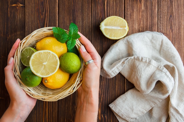 Ensemble de main en tissu blanc tenant le panier de citron et les citrons dans un panier sur une surface en bois. vue de dessus.