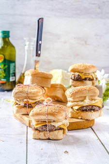 Ensemble de mini hamburgers faits à la main sur une planche à découper en bois et une surface blanche de couteau