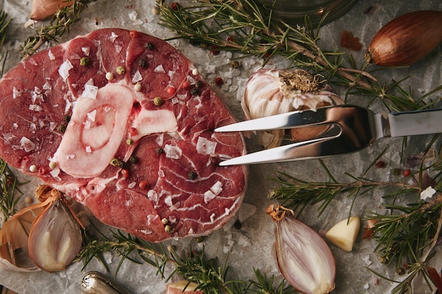 Ensemble de nourriture, oignons, romero, steak de viande crue, sel, poivre, ail, huile d'olive, fourchette. gros plan, vue de dessus