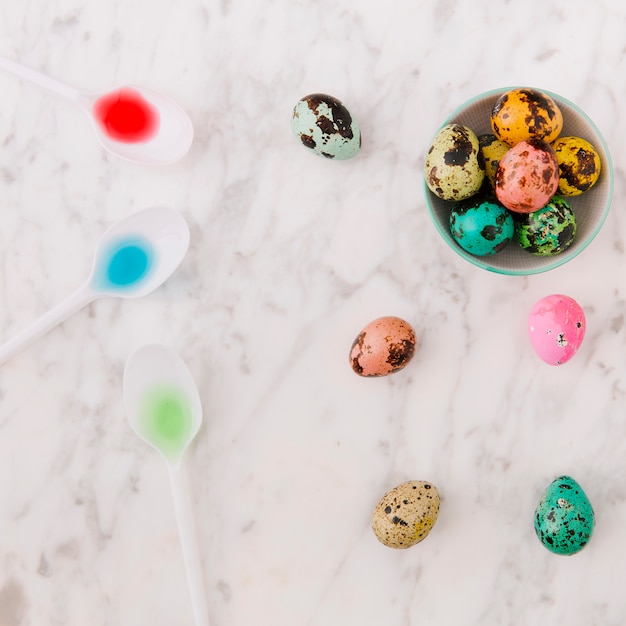 Ensemble d&#39;oeufs de Pâques de caille colorée dans un bol près de cuillère avec des colorants