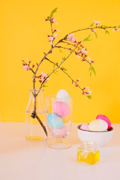 Ensemble d&#39;oeufs de Pâques lumineux près de brindille de fleur dans un vase avec de l&#39;eau et de colorant liquide