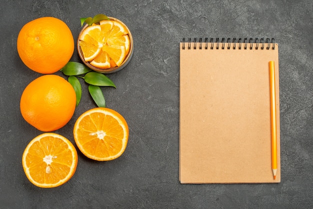 Photo gratuite ensemble d'oranges jaunes entières et hachées et ordinateur portable sur table sombre