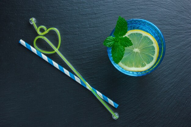 Ensemble de pailles et tranche de citron dans un bol bleu sur une surface en pierre sombre. vue de dessus.