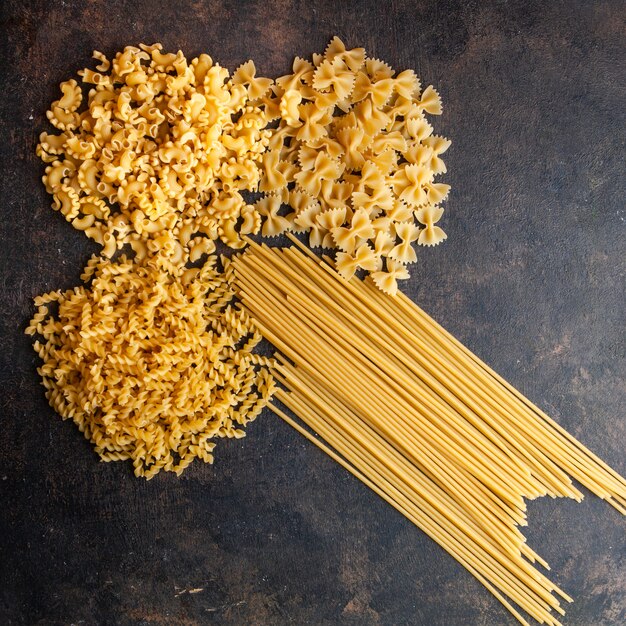 Ensemble de pâtes spaghetti et macaroni sur un fond texturé sombre. vue de dessus.