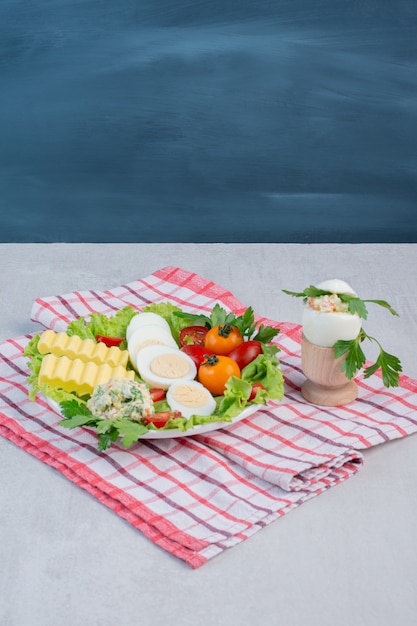 Ensemble de petit-déjeuner de légumes, œufs durs et tranches de beurre sur un plateau sur une serviette sur une table en marbre.