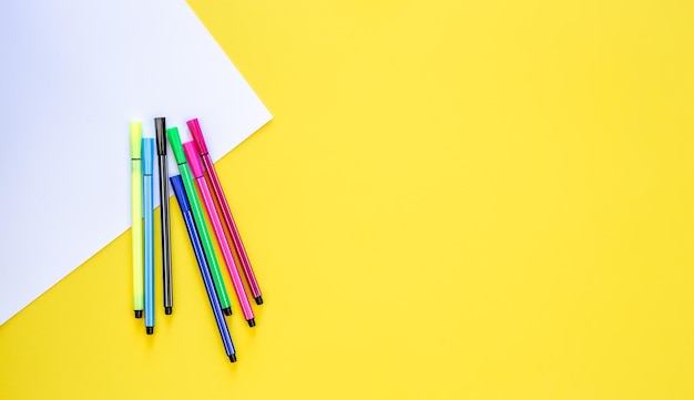 Photo gratuite un ensemble de stylos à pointe de feutre et une feuille de papier blanc sur un fond jaune en haut de l'espace de copie