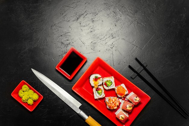 Ensemble de sushis, couteau japonais, baguettes et sur une table en pierre sombre.