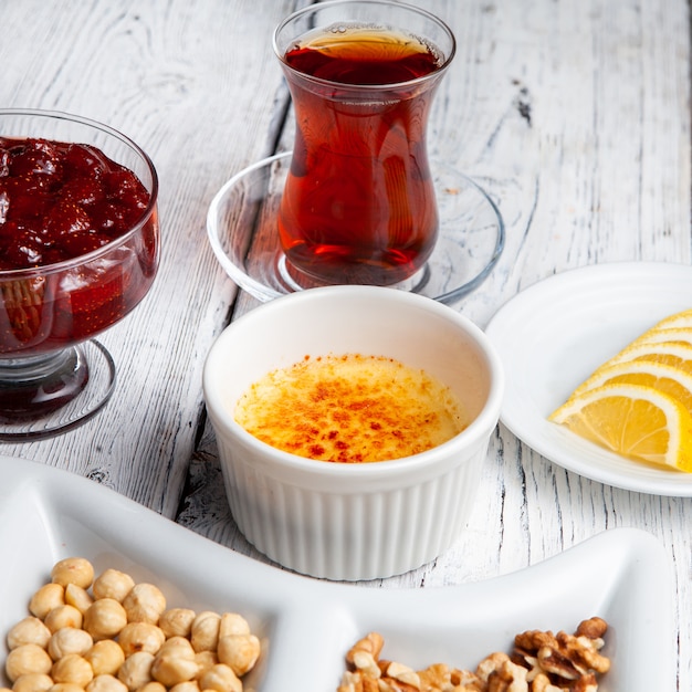 Ensemble de thé, noix, confiture de fruits, citrons en tranches et délicieux dessert dans une assiette sur un fond en bois blanc. vue grand angle.