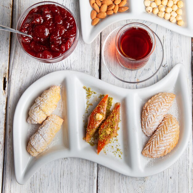 Ensemble de thé, noix, confiture de fruits et délicieux desserts sur un fond en bois blanc. vue de dessus.