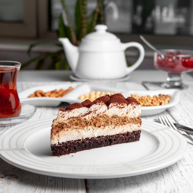 Ensemble de thé, noix, théière, confiture de fruits et délicieux dessert dans une assiette sur un fond en bois blanc. vue de côté.