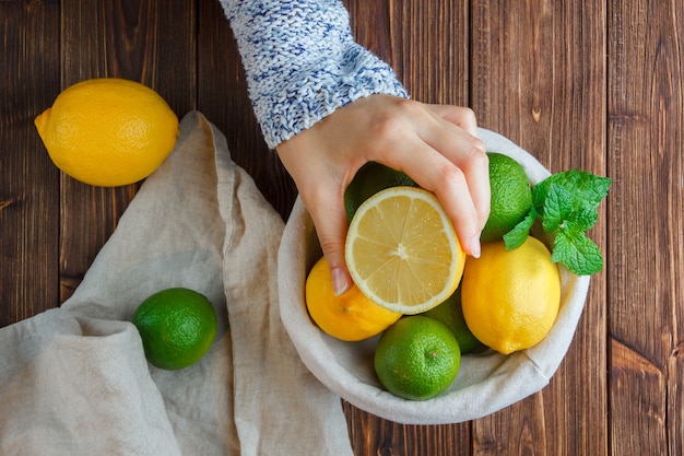 Ensemble de tissu blanc, mains tenant du citron et des citrons dans un panier sur une surface en bois. vue de dessus.