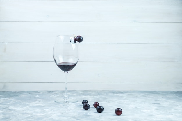 Photo gratuite ensemble d'un verre de vin et de raisins noirs sur fond gris et en bois grungy. vue de côté.