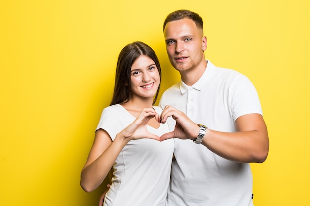 Ensoleillé jeune couple en t-shirts blancs montre signe de coeur avec leurs mains isolées