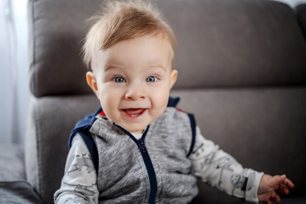 Enthousiaste Bebe Garcon Caucasien Aux Grands Yeux Bleus Assis Sur Un Canape Dans Le Salon Et Souriant Photo Premium