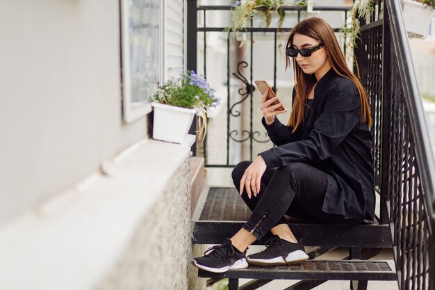 Enthousiaste belle femme brune de bonne humeur utiliser le téléphone à l'extérieur