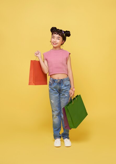 Enthousiaste enfant asiatique heureux, appréciant le shopping, elle porte des sacs à provisions au centre commercial.