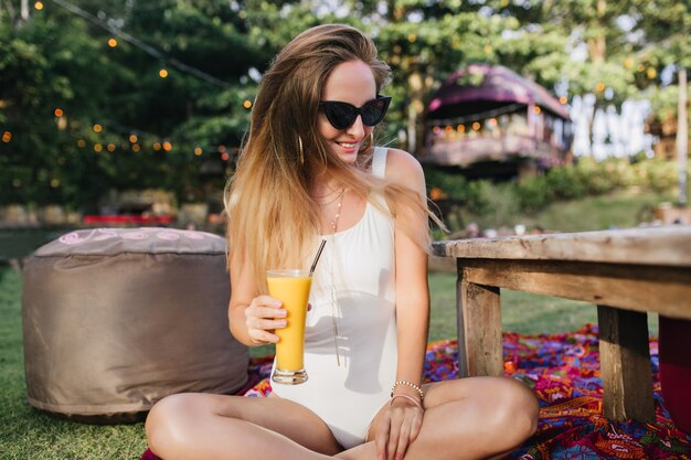 Enthousiaste femme aux cheveux longs bénéficiant d'un cocktail de fruits dans le parc.