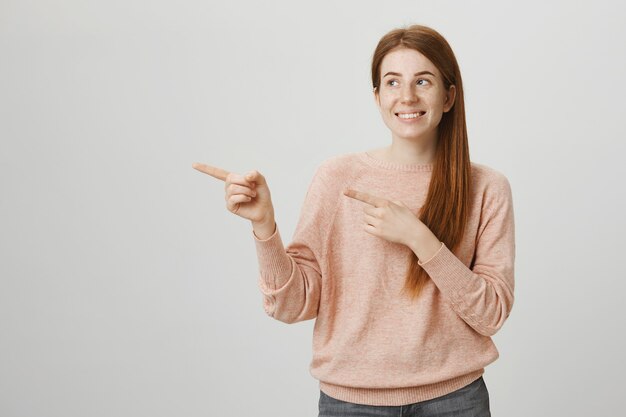 Enthousiaste fille rousse souriante pointant les doigts à gauche