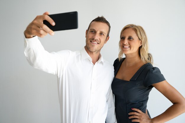 Enthousiaste jeune couple positif posant pour selfie sur smartphone.