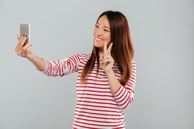 Enthousiaste jeune femme asiatique faire selfie par téléphone