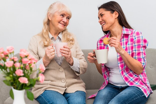 Enthousiaste jeune femme assise avec sa mère tenant une tasse de café